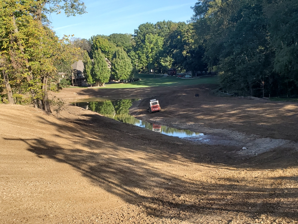 view of a Bobcat on a sloping dirt hillside and small retaining pond view of a Bobcat on a sloping dirt hillside and small retaining pond
