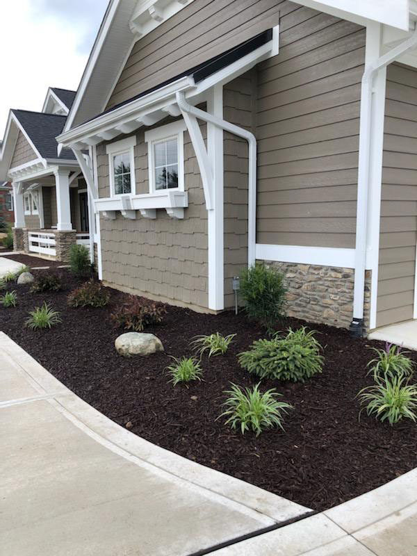 side view of a gray home with white siding; new landscaping that features green shrubs and brown mulch side view of a gray home with white siding; new landscaping that features green shrubs and brown mulch