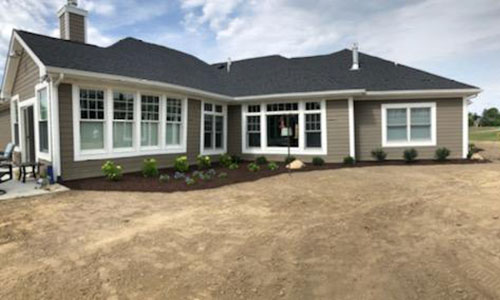 view of back of gray home with new landscaping - green shrubs and brown mulch; yellow grass view of back of gray home with new landscaping - green shrubs and brown mulch; yellow grass