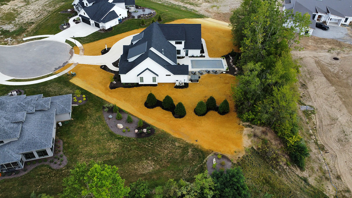 aerial side view of a large white home with a yellow yard and new mature green pine trees and landscaping aerial side view of a large white home with a yellow yard and new mature green pine trees and landscaping